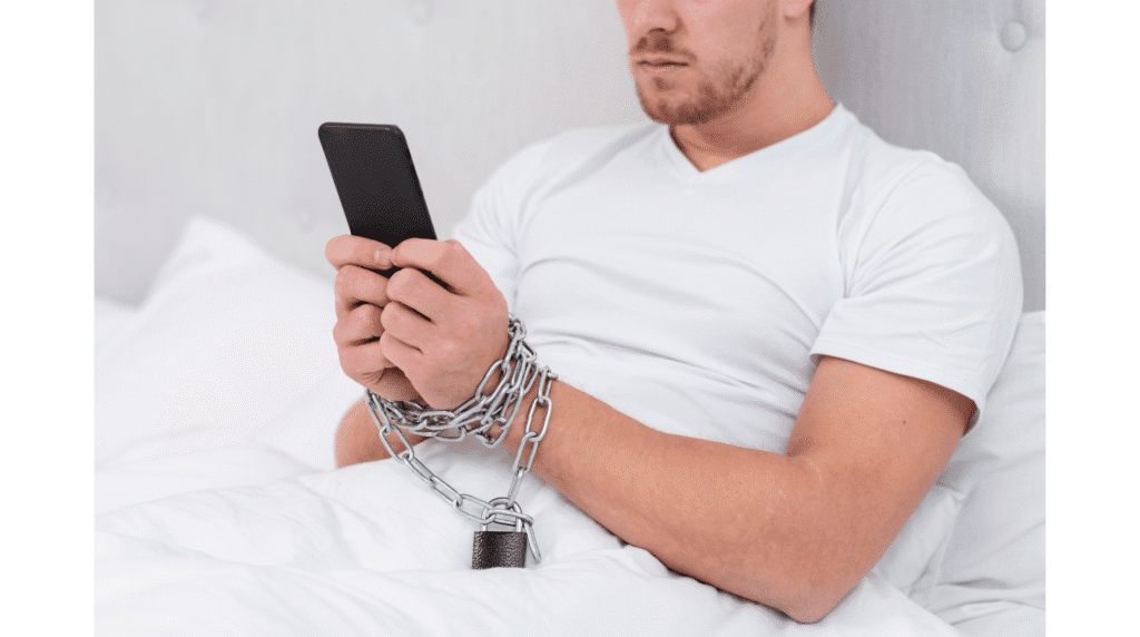 Homem olhando para o telefone enquanto está amarrado com correntes, simbolizando o consumo de pornografia e seus prejuízos.